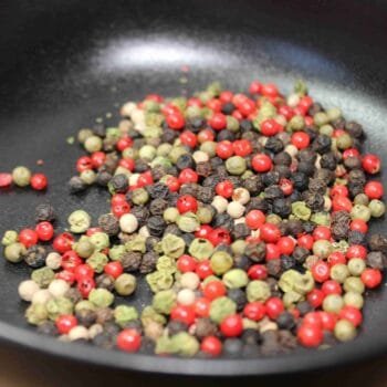 Mélange coloré de grains de poivre dans une poêle, idéal pour rehausser les plats avec une touche épicée et aromatique.