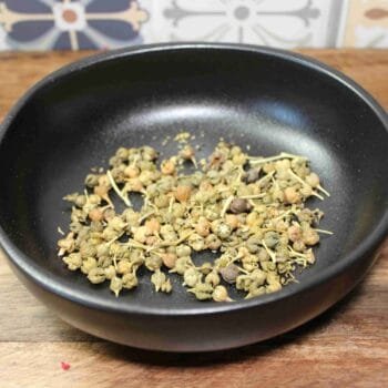 Graines d'ashwagandha séchées dans un bol noir sur une table en bois.