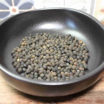 Grains de poivre noir dans un bol en céramique noire, épice aromatique pour la cuisine.