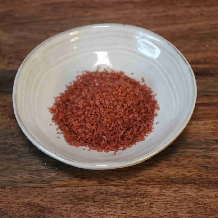 Bol de sel de mer rouge sur une table en bois, idéal pour la cuisine épicée et les plats gourmets.