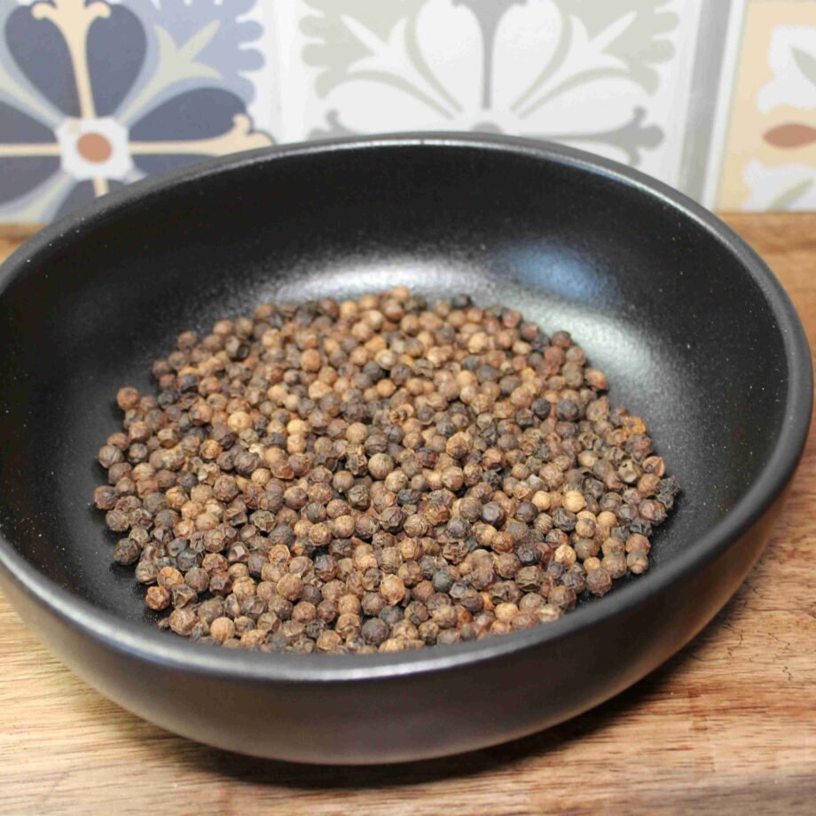 Grains de poivre dans un bol noir sur fond de carreaux colorés dans une cuisine.
