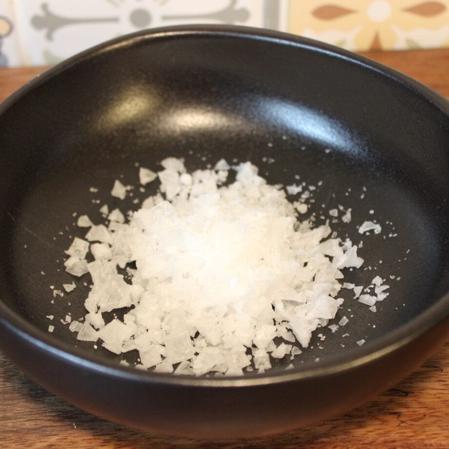 Flocons de sel de mer dans un bol noir, parfaits pour relever vos plats gourmet.