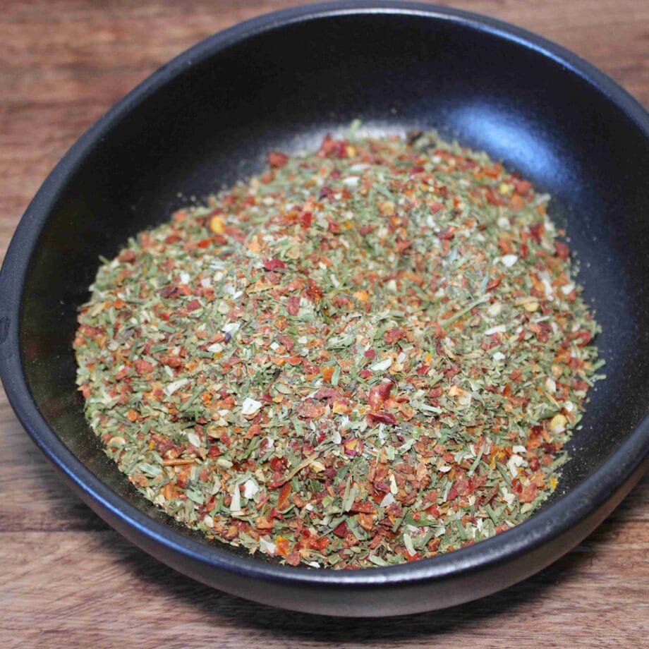 Assaisonnement aux herbes et épices dans un bol noir sur une table en bois.