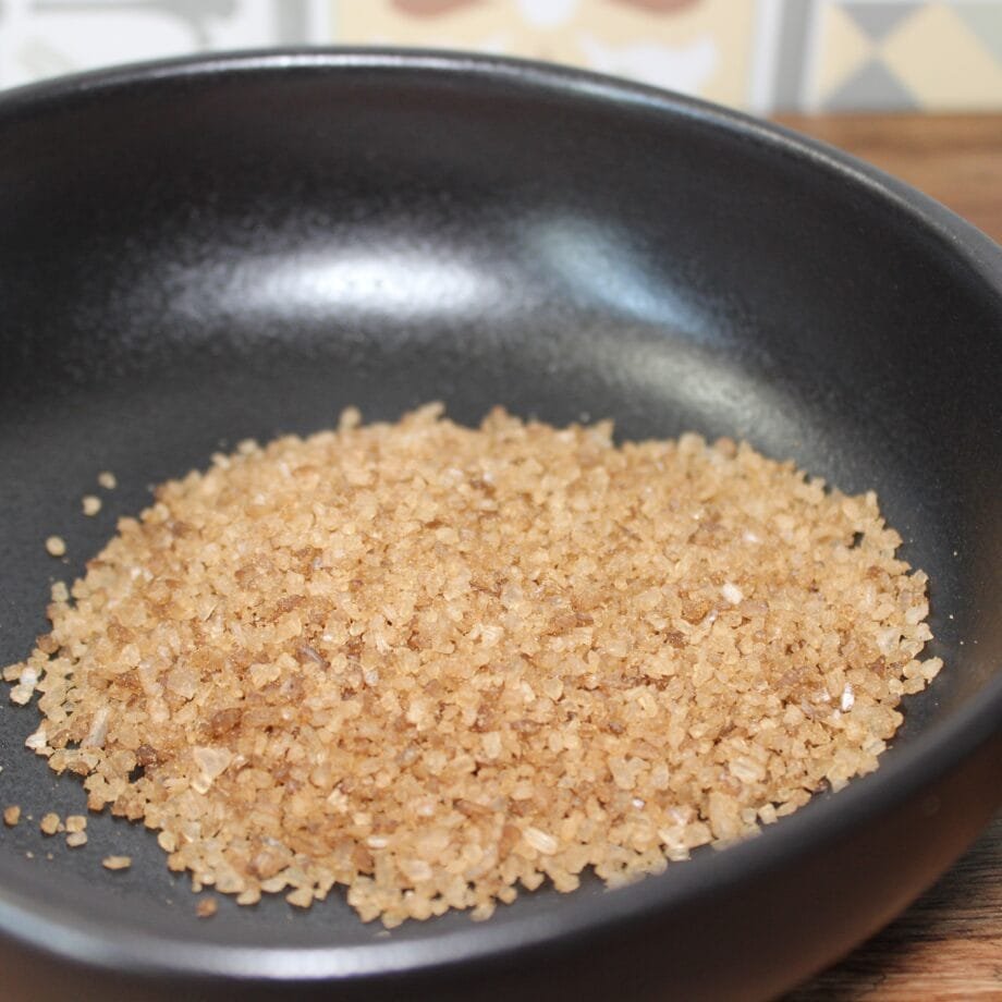 Cristaux de sel brun dans un bol noir sur une table en bois, gros plan sur un condiment naturel et rustique.
