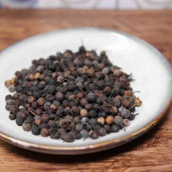 Grains de poivre noir dans une assiette blanche sur une table en bois, prêts pour la cuisine aromatique.