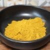 Poudre d'épices jaune vif dans un bol noir, idéale pour la cuisine exotique et recettes savoureuses.