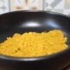 Poudre de curry jaune dans un bol noir sur table en bois, avec carrelage en arrière-plan.