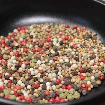 Mélange coloré de grains de poivre et épices variées dans une poêle noire, idéal pour aromatiser vos plats.