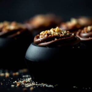 Cupcakes au chocolat garnis de glaçage crémeux et de noix concassées sur fond sombre.