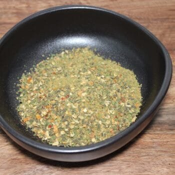 Assaisonnement épicé dans un bol noir sur une table en bois, idéal pour rehausser vos plats faits maison.