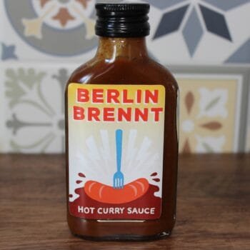 Bouteille de sauce curry épicée Berlin Brennt sur fond coloré. Idéale pour relever vos plats.