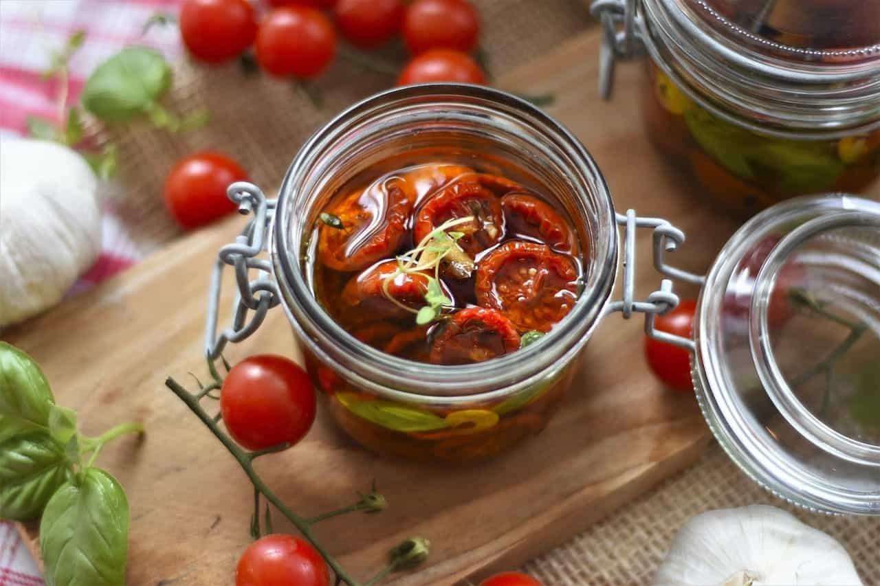 Tomates séchées marinées dans un bocal en verre sur planche en bois, entouré de basilic et d'ail.