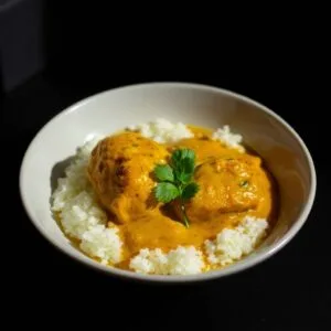 Curry crémeux sur lit de riz basmati, décoré de coriandre fraîche. Plat indien savoureux et aromatique.