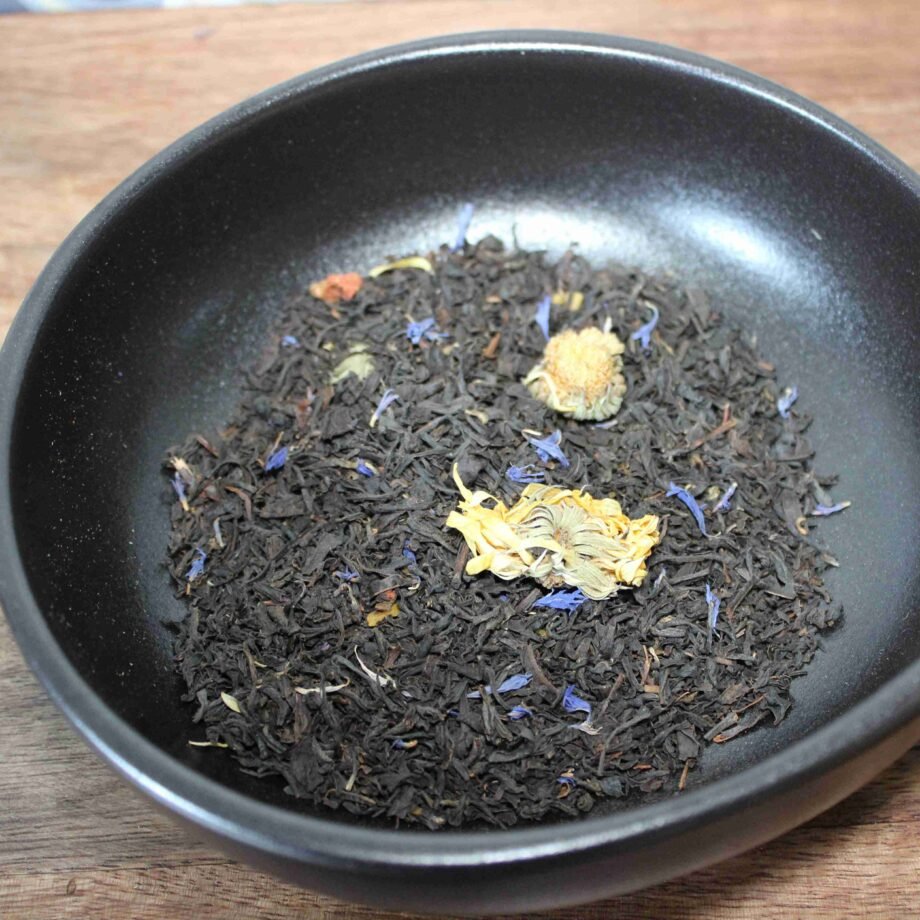 Thé noir en vrac aux fleurs séchées, présenté dans un bol noir sur une table en bois.