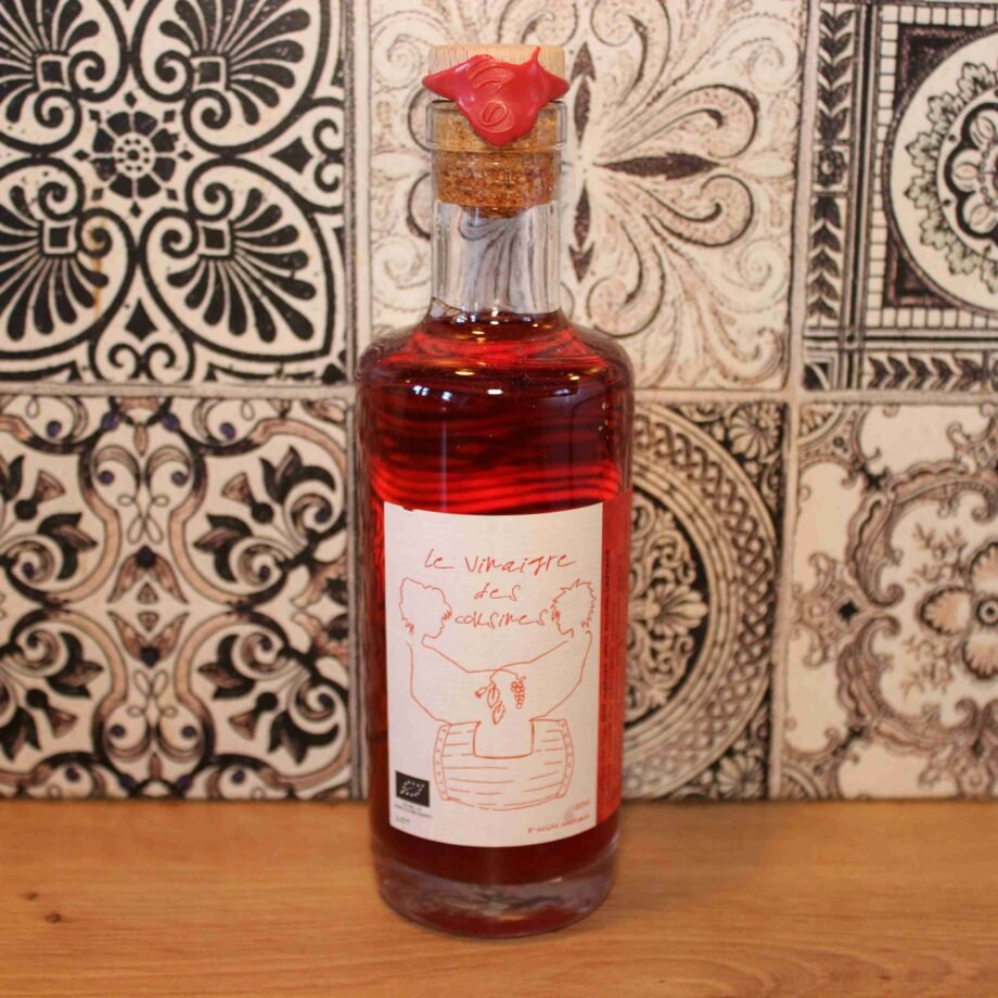 Bouteille de vinaigre artisanale rouge sur fond de carreaux décoratifs en céramique, étiquette dessinée à la main.