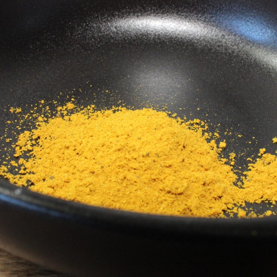 Poudre jaune épicée dans un bol noir, idéale pour agrémenter vos plats de saveurs exotiques et colorées.