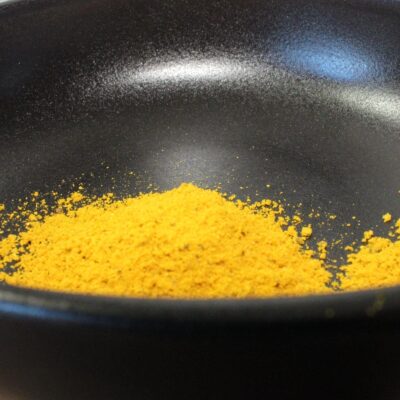 Poudre de curry jaune dans un bol noir, parfait pour ajouter de la saveur aux plats.