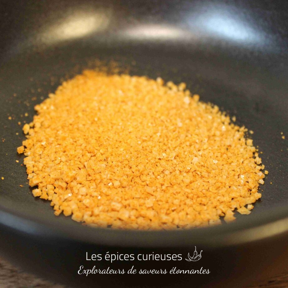 Poudre jaune dans un bol noir, utilisée en cuisine pour ajouter du goût et de la texture aux plats.