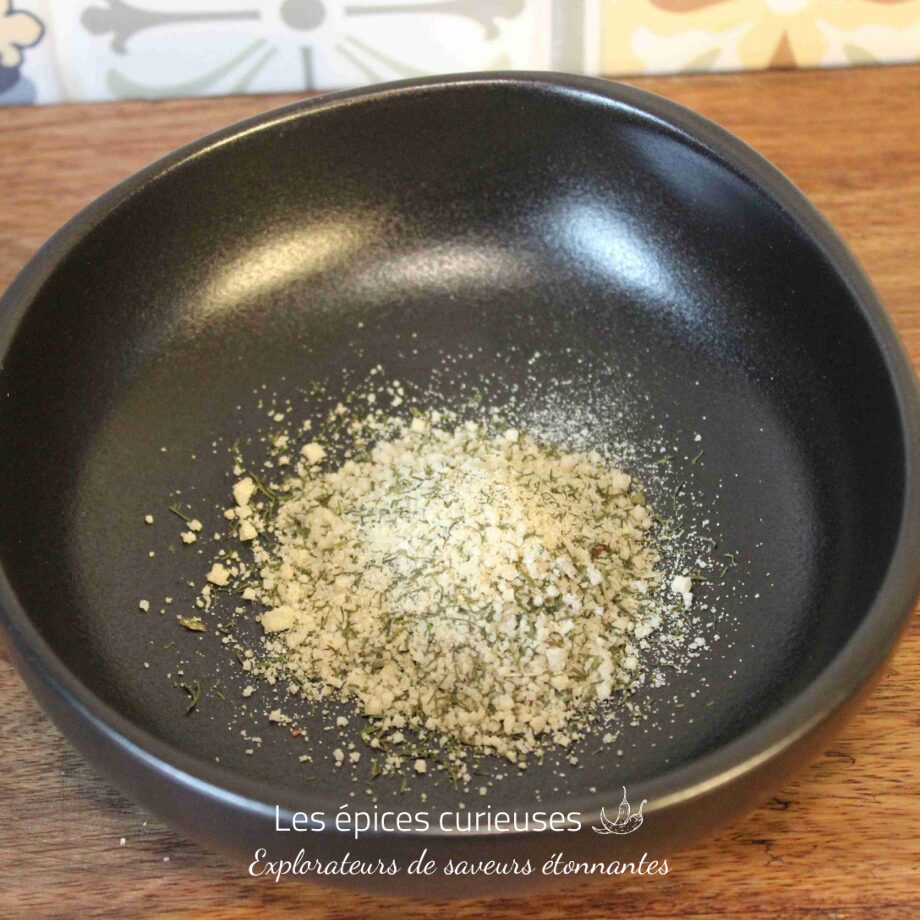 Assiette noire avec parmesan râpé et herbes, posée sur une table en bois, décor mural coloré en arrière-plan.