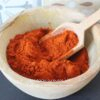 Bol en bois rempli de paprika rouge en poudre avec une cuillère en bois, sur fond de motif coloré.