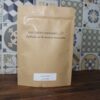 Sachet de poudre d'ananas des Épices Curieuses, fond carrelage coloré, saveurs étonnantes à explorer.