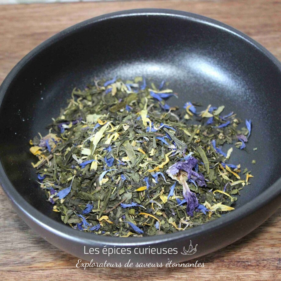 Mélange de thé vert et fleurs séchées dans un bol noir sur table en bois, prêt pour une infusion parfumée et colorée.