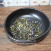 Bol de tisane aux fleurs séchées colorées sur planche en bois, fond carrelé.