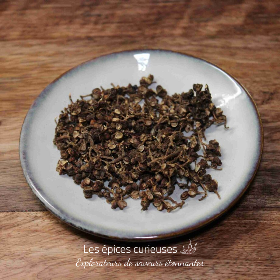 Baies de Sichuan séchées sur une assiette blanche, posée sur une table en bois.