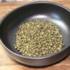 Grains de poivre vert dans un bol noir, posés sur une surface en bois.