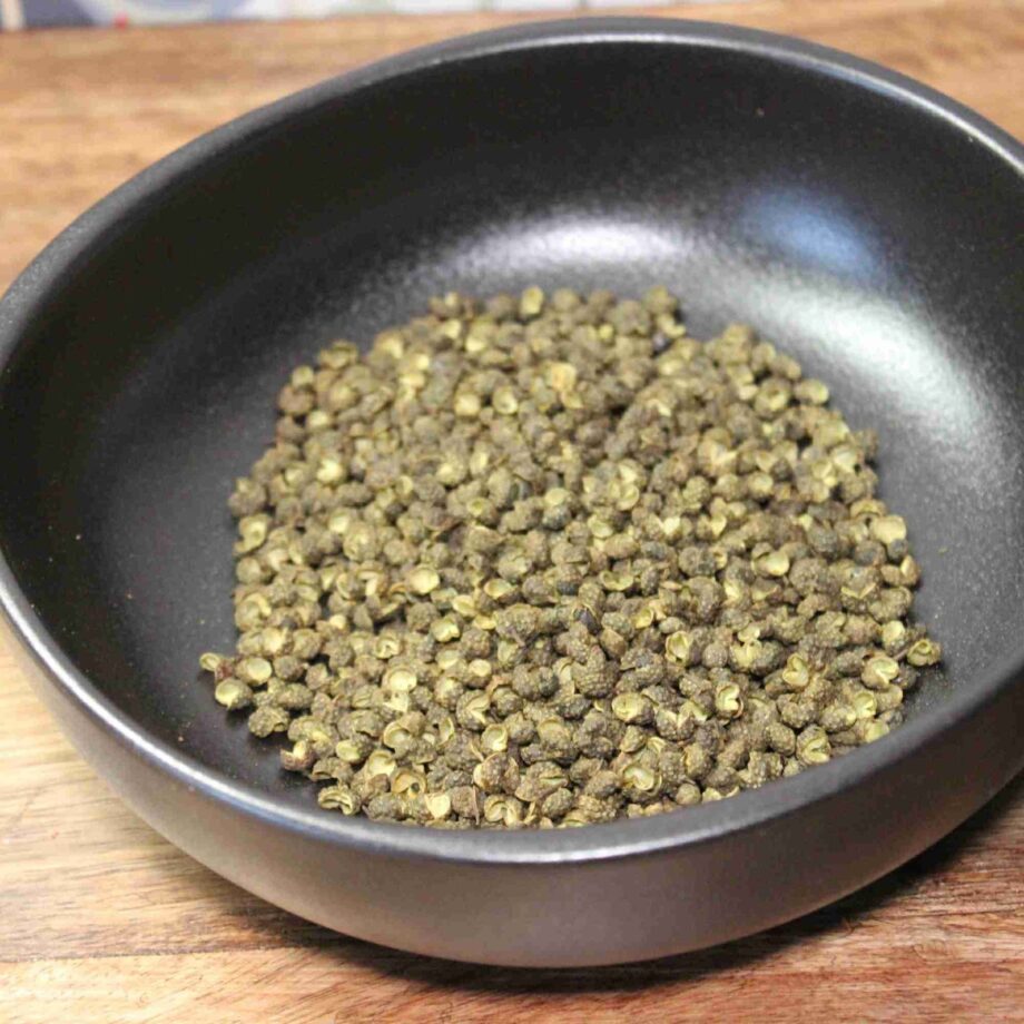 Grains de poivre vert dans un bol noir, posés sur une surface en bois.