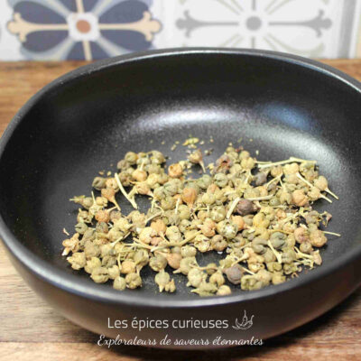Graines séchées dans un bol noir sur une table en bois, avec des carreaux décoratifs en fond.