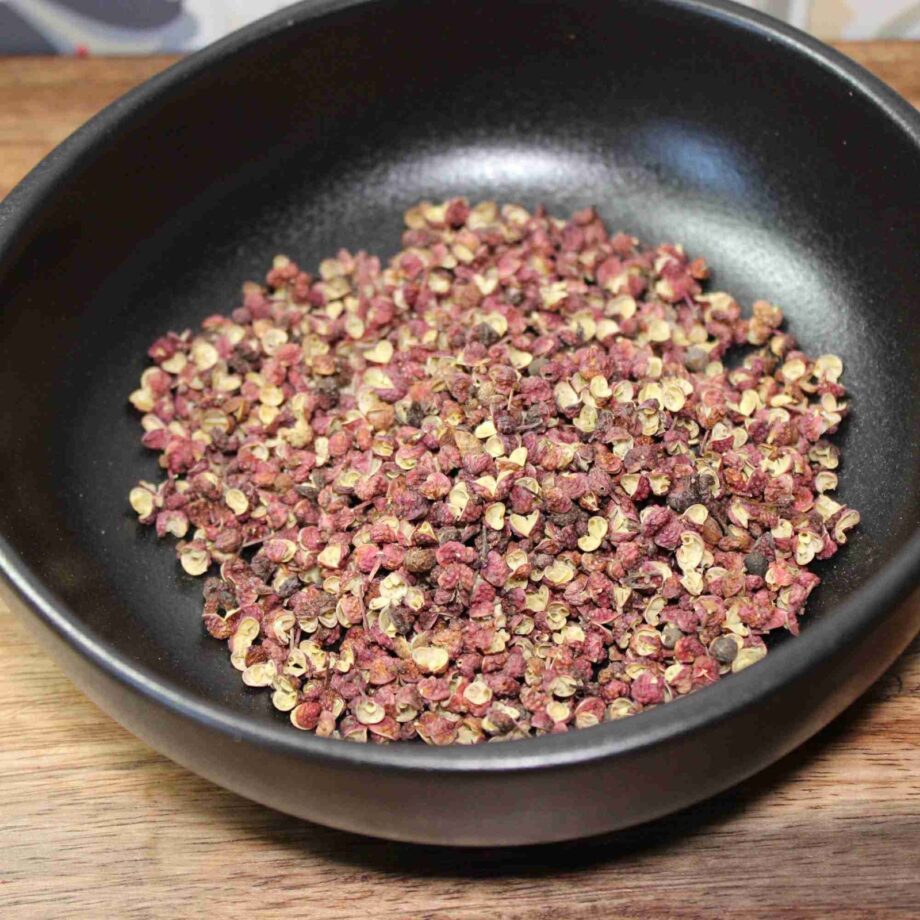 Grains de poivre de Sichuan dans un bol noir sur une table en bois, prêts à être utilisés en cuisine asiatique.