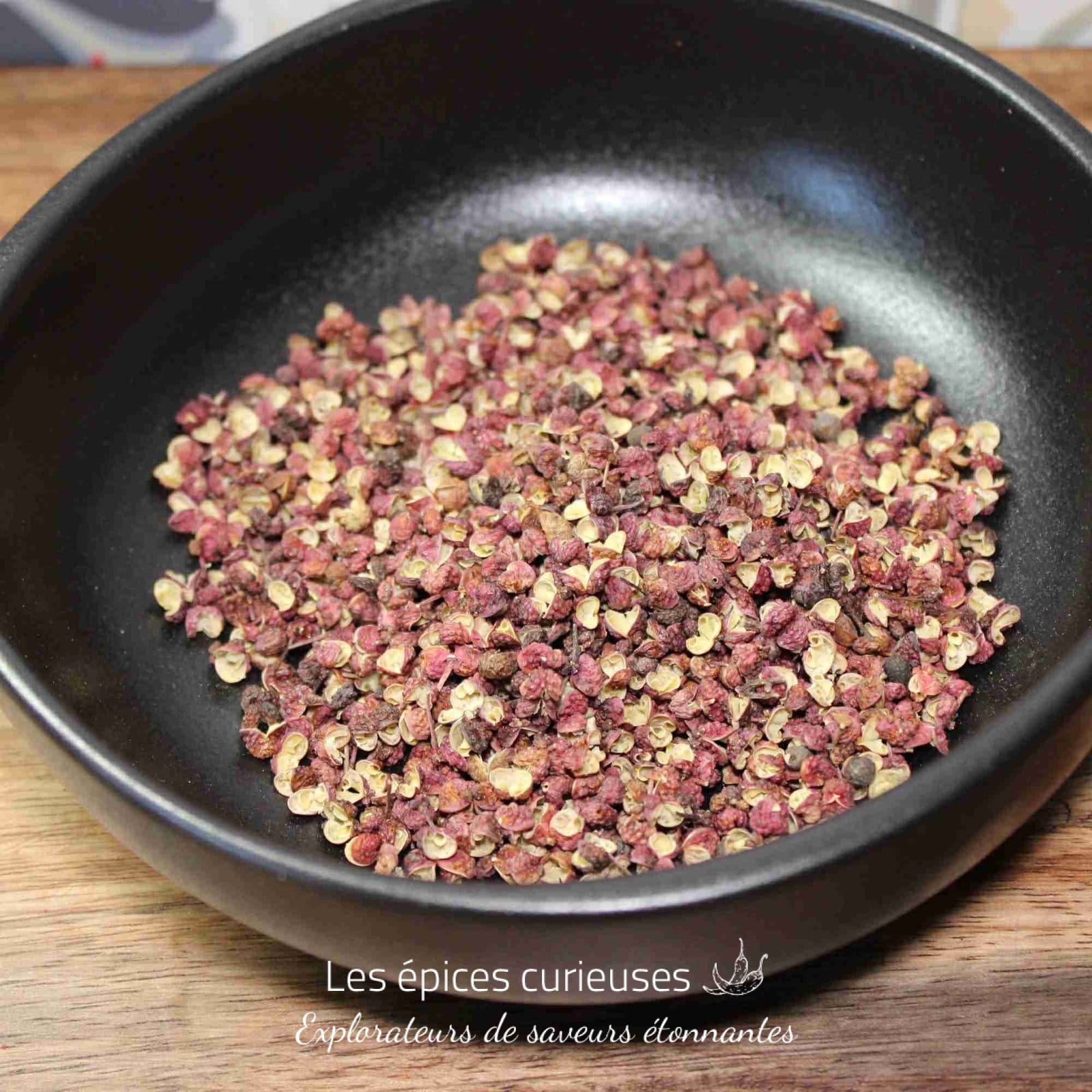Grains de poivre de Sichuan dans un bol noir sur une table en bois, prêts à être utilisés en cuisine asiatique.