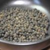 Grains de poivre noir entiers dans une poêle, prêts à être utilisés en cuisine pour aromatiser vos plats.