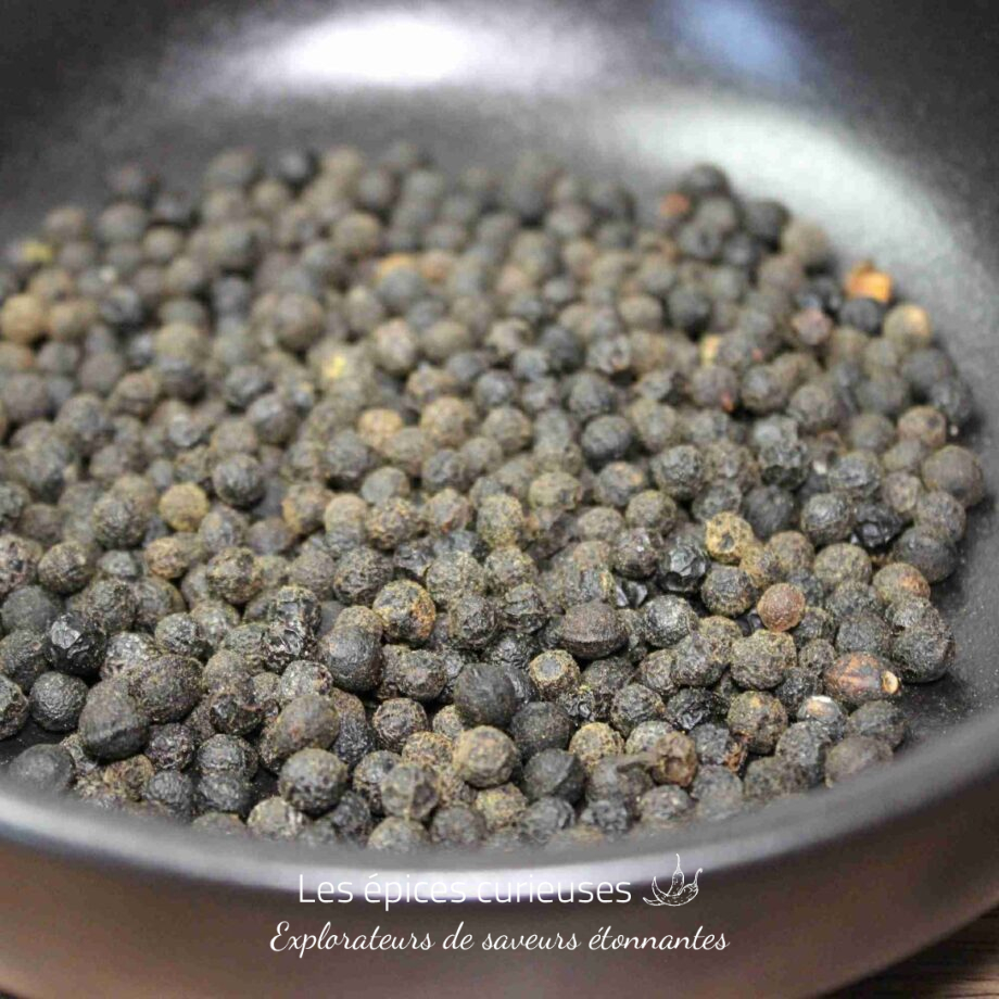 Grains de poivre noir entiers dans une poêle, prêts à être utilisés en cuisine pour aromatiser vos plats.