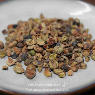 Graines de cardamome séchées posées sur une assiette blanche, épice aromatique utilisée en cuisine et pâtisserie.