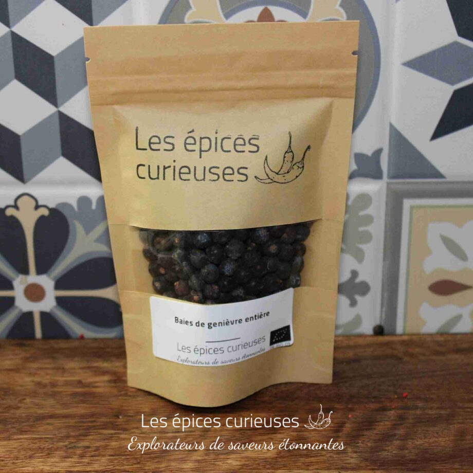 Paquet de baies de genièvre entières Les épices curieuses sur une table en bois avec fond de carreaux colorés.