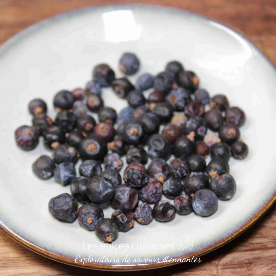 Baies de genièvre séchées sur une assiette blanche, utilisées pour assaisonner divers plats et boissons.