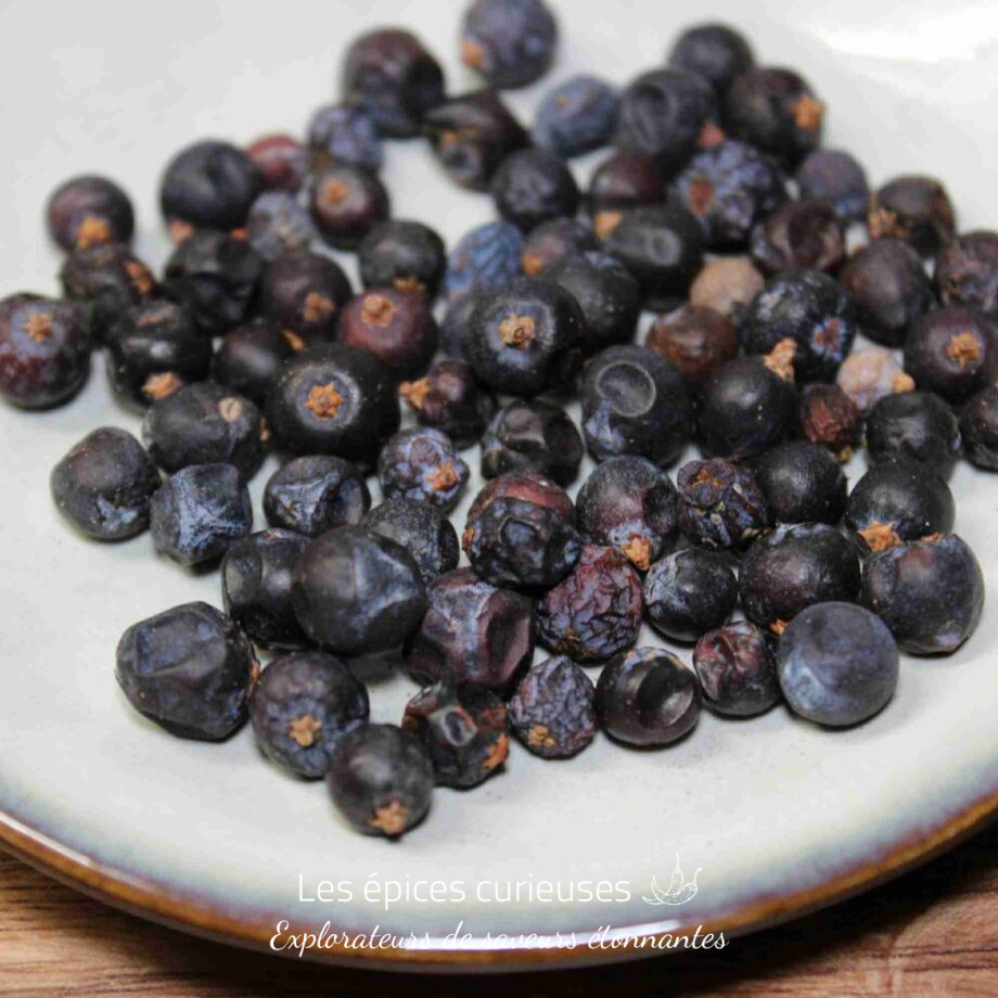 Baies de genièvre séchées sur une assiette blanche, idéales pour aromatiser plats et boissons.