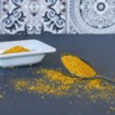 Spoonful of Sambahara curry spice with spilled powder on dark surface.
