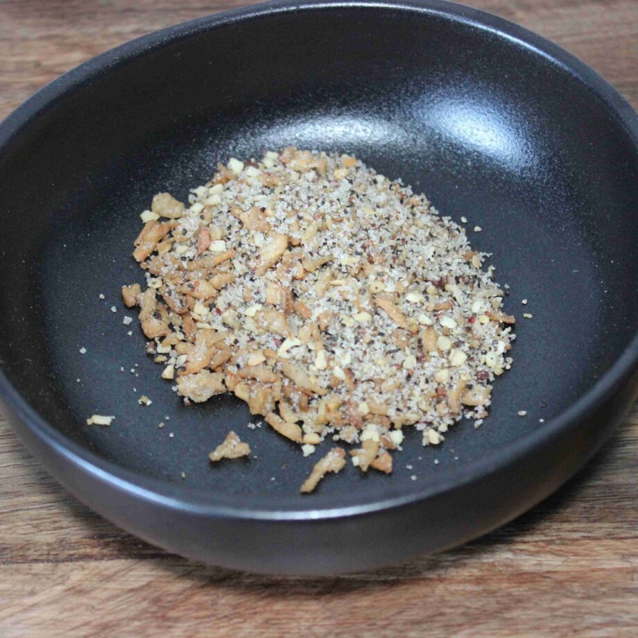 Mélange de noix concassées dans un bol noir sur une surface en bois.