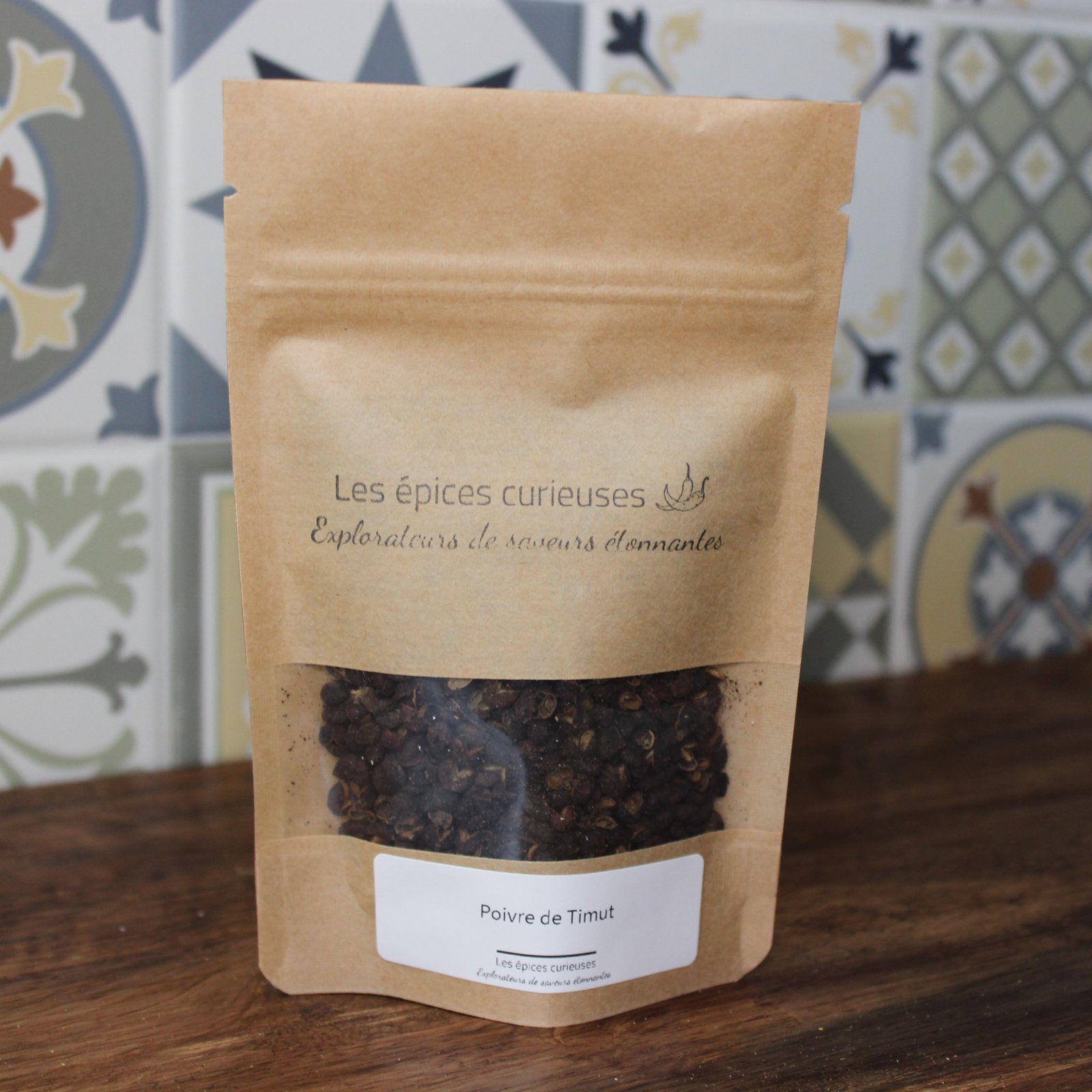 Poivre de Timut en sachet kraft, épices exotiques sur fond de carreaux colorés. Parfait pour agrémenter vos plats.