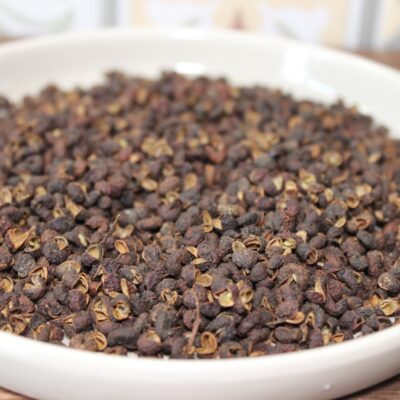 Grains de poivre de Sichuan dans un bol blanc, utilisés en cuisine asiatique pour leur saveur unique et épicée.