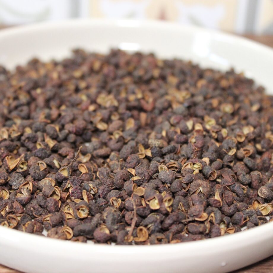 Grains de poivre de Sichuan dans un bol blanc, utilisés en cuisine asiatique pour leur saveur unique et épicée.