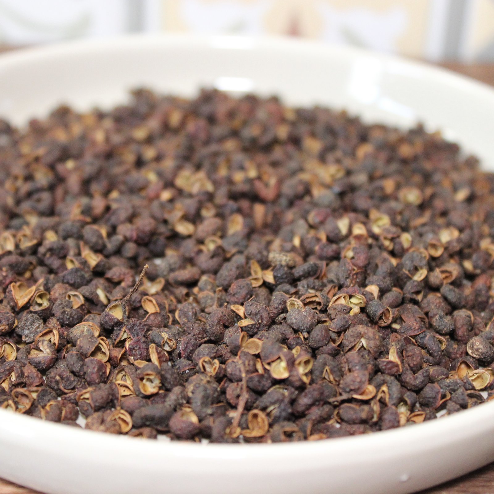 Grains de poivre de Sichuan dans un bol blanc, utilisés en cuisine asiatique pour leur saveur unique et épicée.