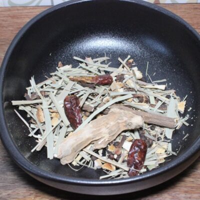 Assortiment d'herbes séchées et épices dans un bol noir, idéal pour préparer des infusions ou assaisonner des plats.