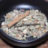 Mélange d'épices séchées dans un bol noir, avec bâton de cannelle et cardamome pour infusion parfumée.