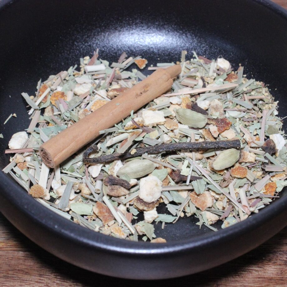 Mélange d'épices séchées dans un bol noir, avec bâton de cannelle et cardamome pour infusion parfumée.