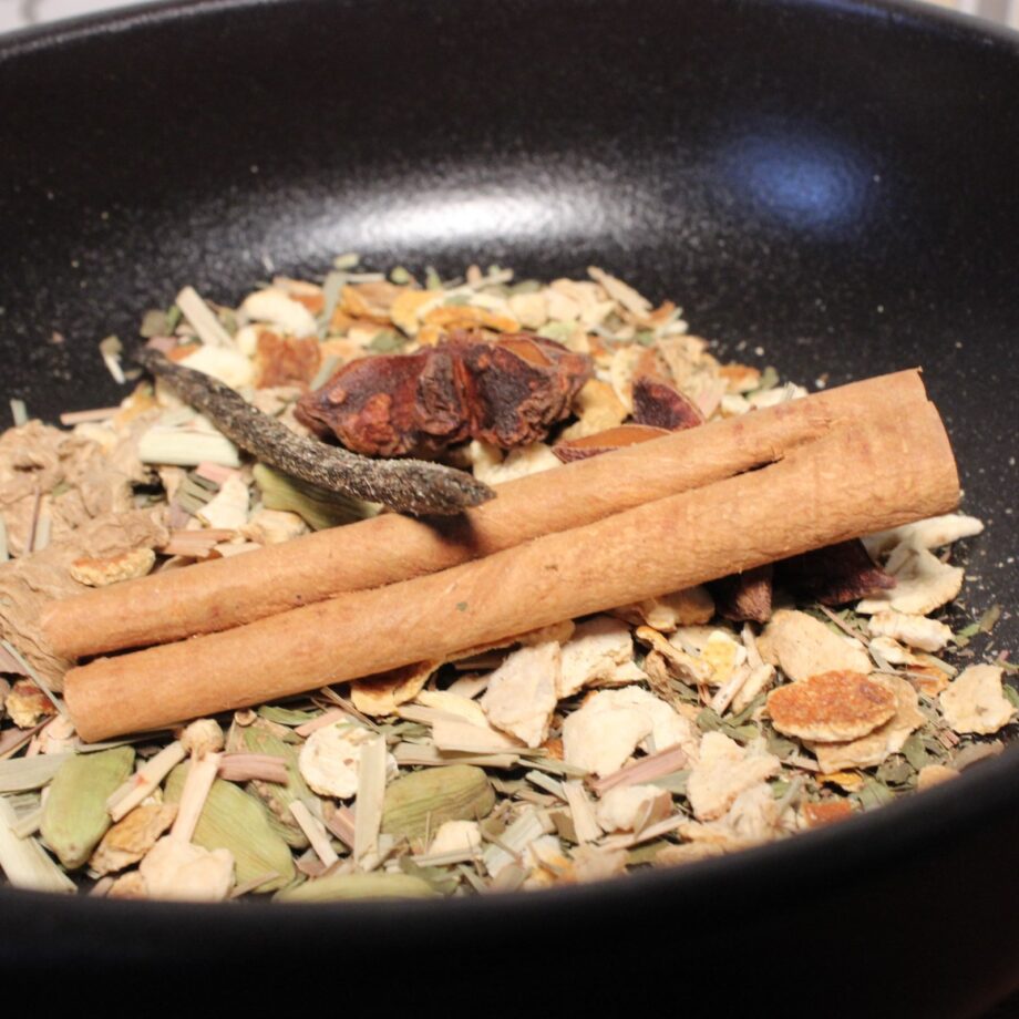 Mélange d'épices en vrac avec bâton de cannelle dans une poêle noire. Parfait pour infusions ou cuisine exotique.
