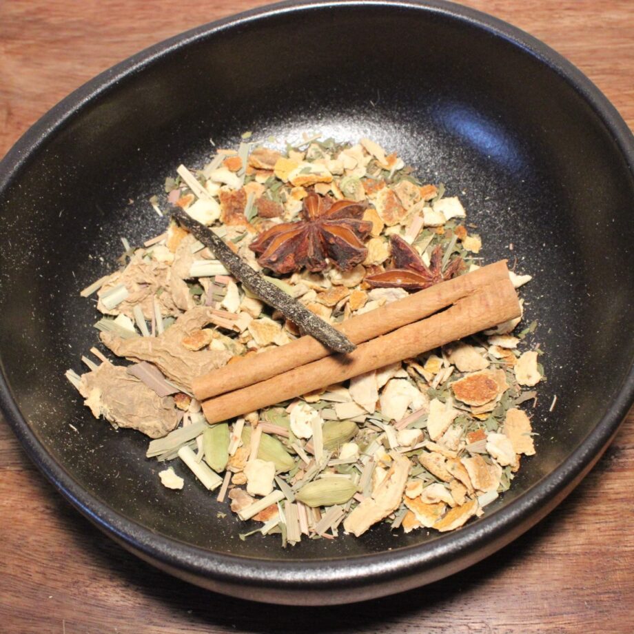 Mélange d'épices variées dans un bol noir, incluant cannelle et anis étoilé, sur fond de table en bois.